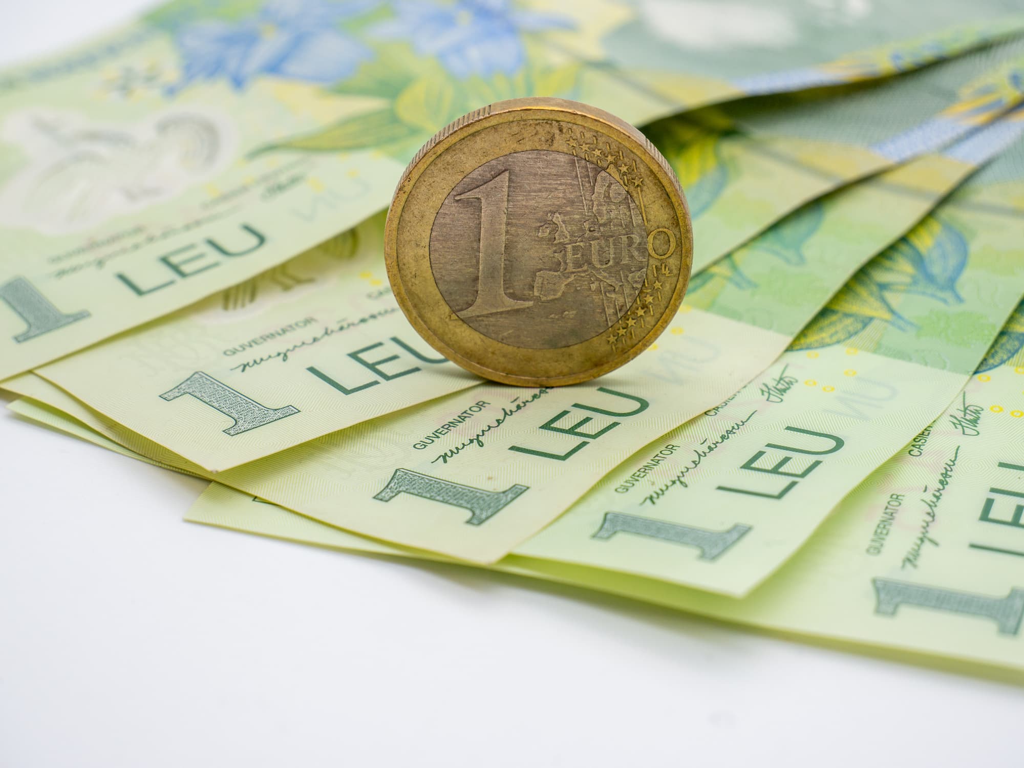 One euro coin on several one leu banknotes.